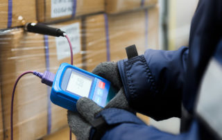 Hands of a worker using a thermometer to measure the temperature of food inside boxes.